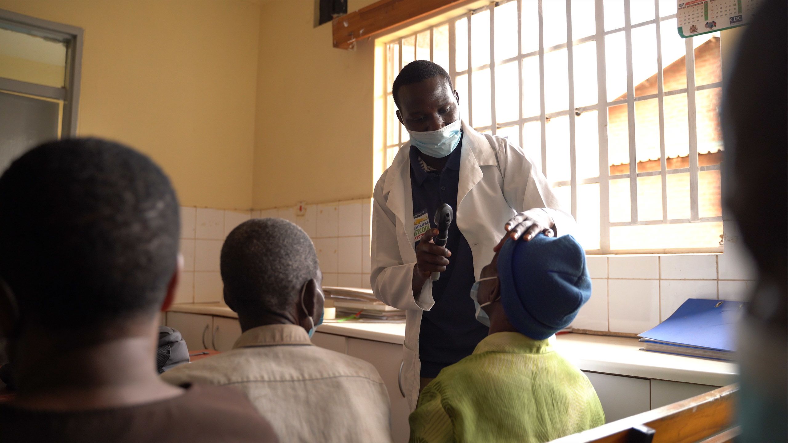 Inside the health centre George screens a woman's eyes with an ophthalmoscope.