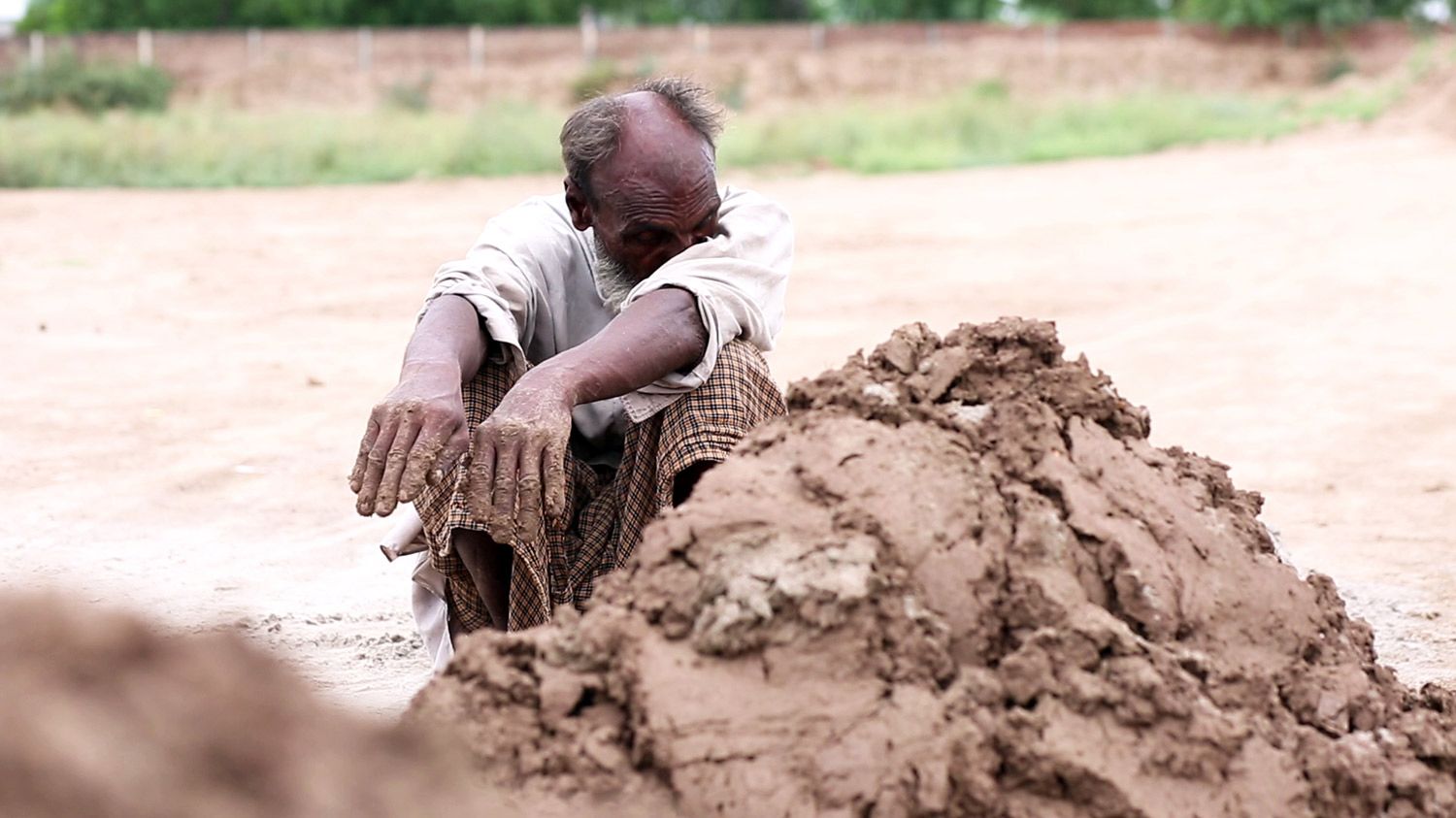 A man rubs his eyes on his upper arm while making bricks.
