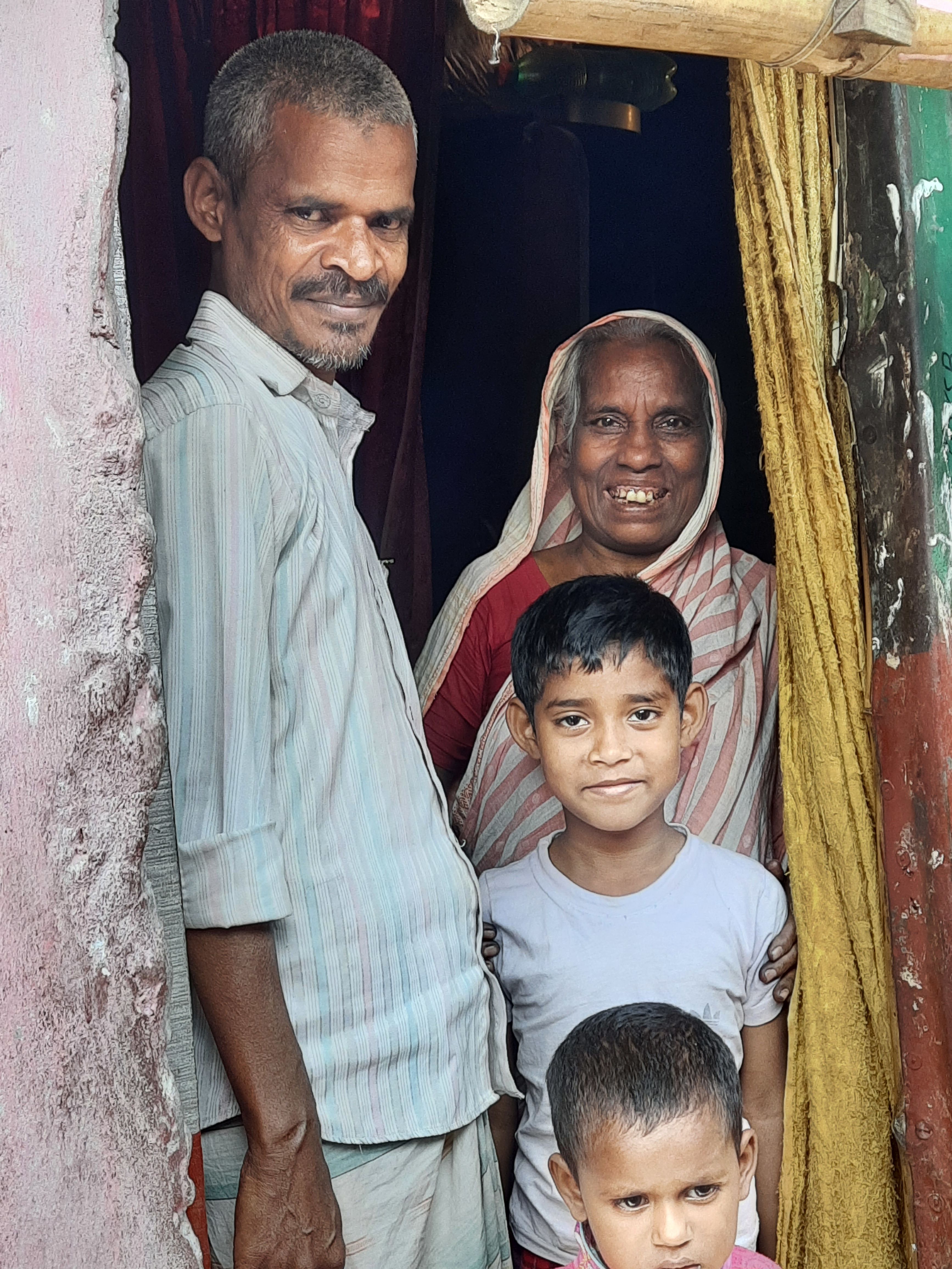 Hasina smiling in her home with her son and grandchildren.